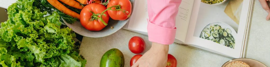 Top view of fresh vegetables and hands arranging them with a recipe book, promoting healthy eating.